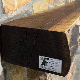 A live edge style fireplace mantel, made from walnut wood, mounted to a rock wall.