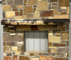 A live edge style fireplace mantel, made from walnut wood, mounted to a rock wall.