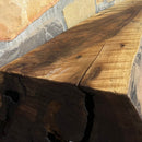 A live edge style fireplace mantel, made from walnut wood, mounted to a rock wall.