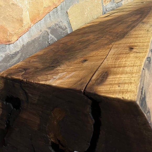 A live edge style fireplace mantel, made from walnut wood, mounted to a rock wall.