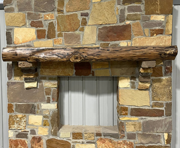 A live edge style fireplace mantel, made from walnut wood, mounted to a rock wall.