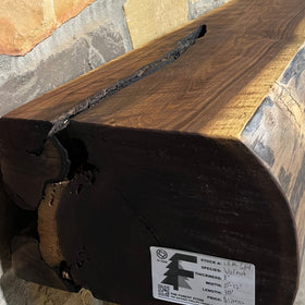 A live edge style fireplace mantel, made from walnut wood, mounted to a rock wall.