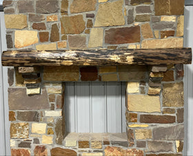 A live edge style fireplace mantel, made from walnut wood, mounted to a rock wall.