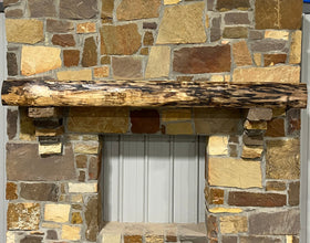 A live edge style fireplace mantel, made from walnut wood, mounted to a rock wall.