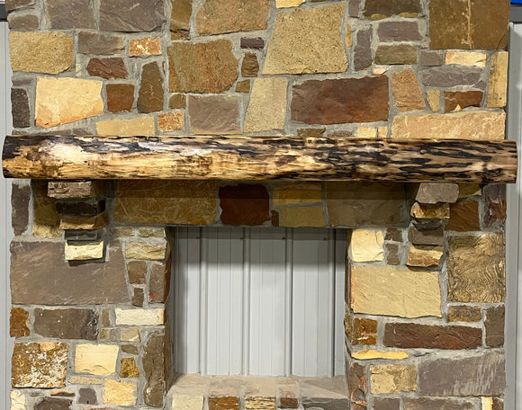 A live edge style fireplace mantel, made from walnut wood, mounted to a rock wall.