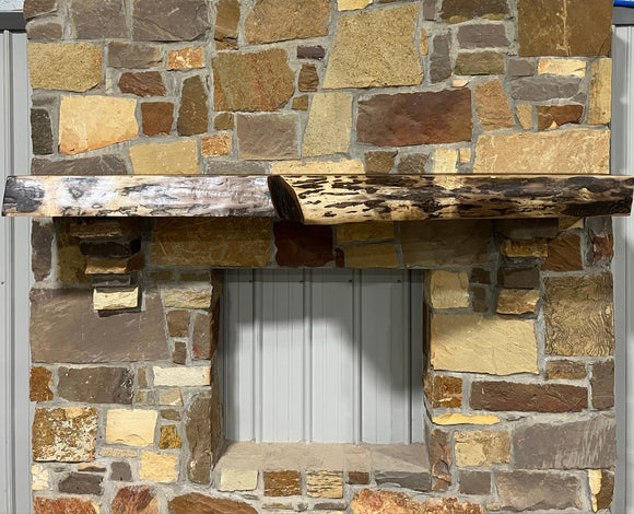 A live edge style fireplace mantel, made from walnut wood, mounted to a rock wall.
