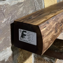 A live edge style fireplace mantel, made from walnut wood, mounted to a rock wall.