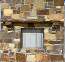 A live edge style fireplace mantel, made from walnut wood, mounted to a rock wall.