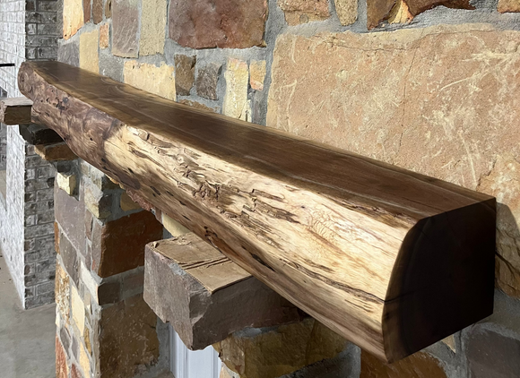 A live edge style fireplace mantel, made from walnut wood, mounted to a rock wall.