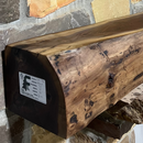 A live edge style fireplace mantel, made from walnut wood, mounted to a rock wall.