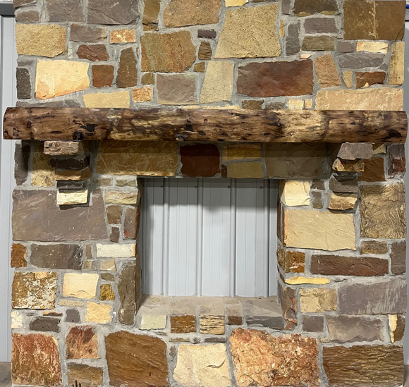 A live edge style fireplace mantel, made from walnut wood, mounted to a rock wall.