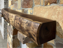 A live edge style fireplace mantel, made from walnut wood, mounted to a rock wall.