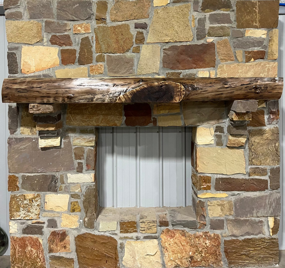 A live edge style fireplace mantel, made from walnut wood, mounted to a rock wall.