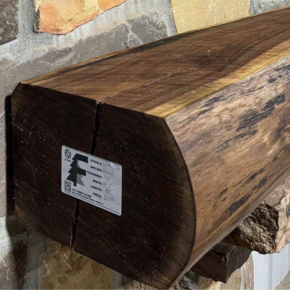 A live edge style fireplace mantel, made from walnut wood, mounted to a rock wall.