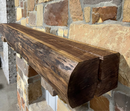 A live edge style fireplace mantel, made from walnut wood, mounted to a rock wall.