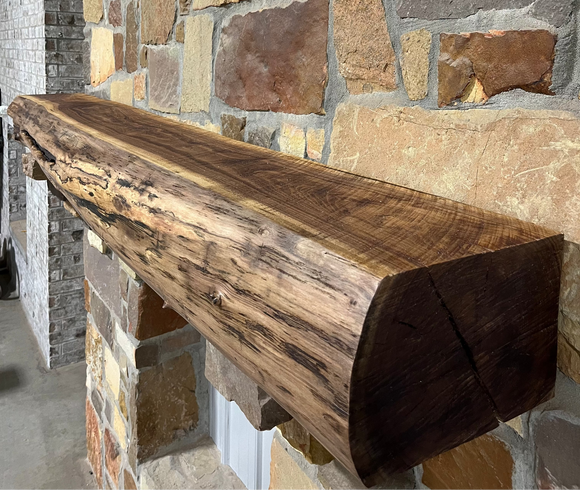 A live edge style fireplace mantel, made from walnut wood, mounted to a rock wall.