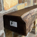 A live edge style fireplace mantel, made from walnut wood, mounted to a rock wall.