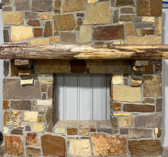 A live edge style fireplace mantel, made from walnut wood, mounted to a rock wall.