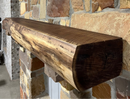 A live edge style fireplace mantel, made from walnut wood, mounted to a rock wall.