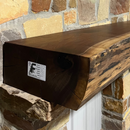 A live edge style fireplace mantel, made from walnut wood, mounted to a rock wall.
