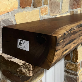 A live edge style fireplace mantel, made from walnut wood, mounted to a rock wall.