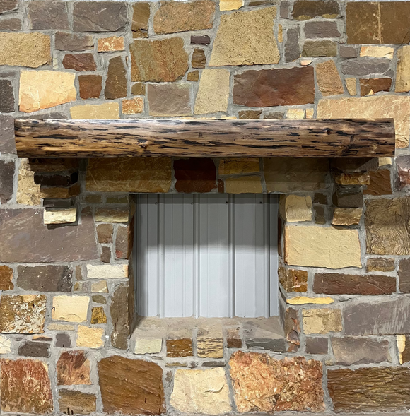 A live edge style fireplace mantel, made from walnut wood, mounted to a rock wall.