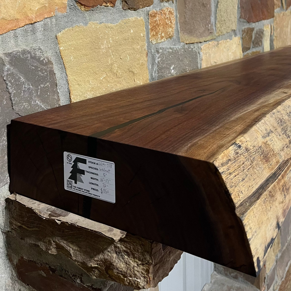 A live edge style fireplace mantel, made from walnut wood, mounted to a rock wall.