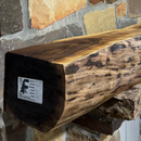 A live edge style fireplace mantel, made from walnut wood, mounted to a rock wall.