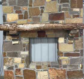 A live edge style fireplace mantel, made from walnut wood, mounted to a rock wall.