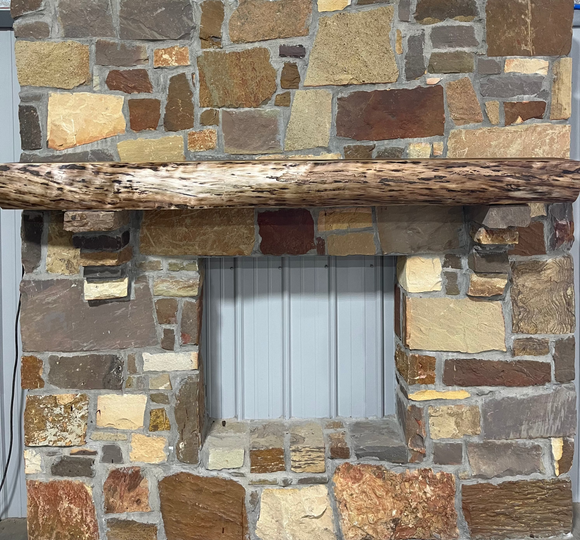 A live edge style fireplace mantel, made from walnut wood, mounted to a rock wall.