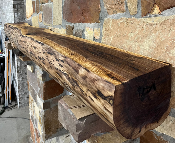 A live edge style fireplace mantel, made from walnut wood, mounted to a rock wall.