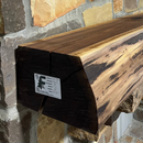 A live edge style fireplace mantel, made from walnut wood, mounted to a rock wall.