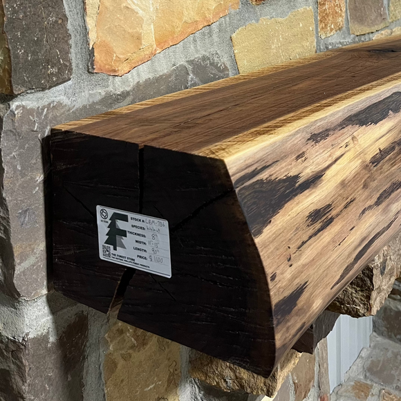 A live edge style fireplace mantel, made from walnut wood, mounted to a rock wall.