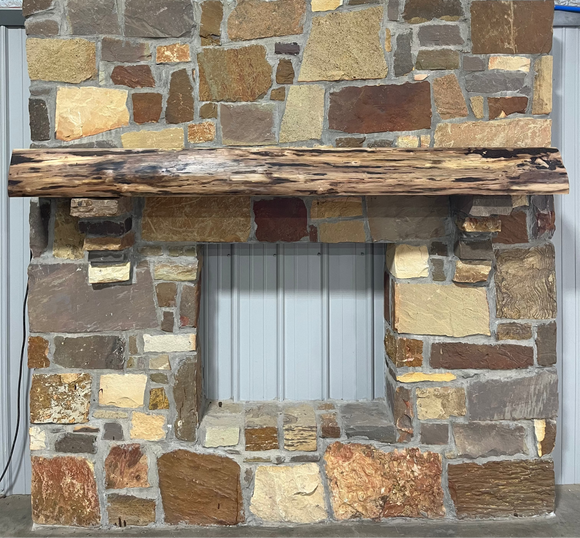 A live edge style fireplace mantel, made from walnut wood, mounted to a rock wall.