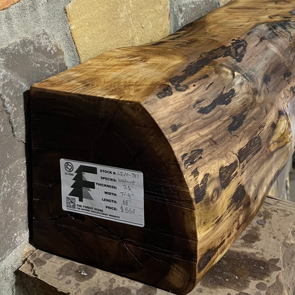 A live edge style fireplace mantel, made from walnut wood, mounted to a rock wall.