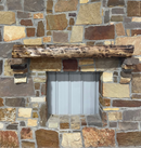 A live edge style fireplace mantel, made from walnut wood, mounted to a rock wall.
