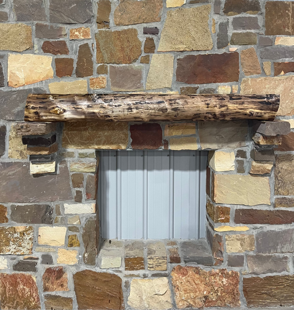 A live edge style fireplace mantel, made from walnut wood, mounted to a rock wall.
