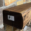 A live edge style fireplace mantel, made from walnut wood, mounted to a rock wall.