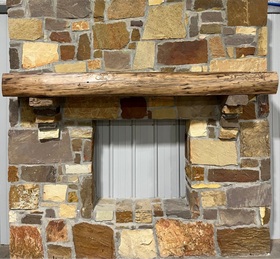A live edge style fireplace mantel, made from walnut wood, mounted to a rock wall.
