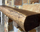 A live edge style fireplace mantel, made from walnut wood, mounted to a rock wall.
