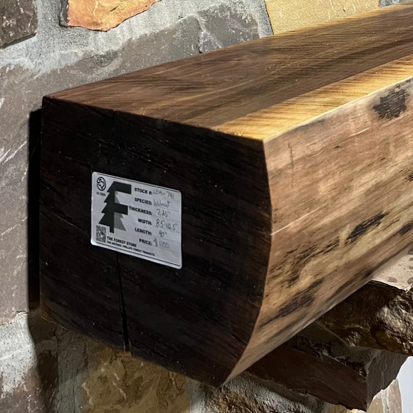 A live edge style fireplace mantel, made from walnut wood, mounted to a rock wall.