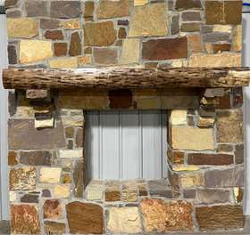 A live edge style fireplace mantel, made from walnut wood, mounted to a rock wall.