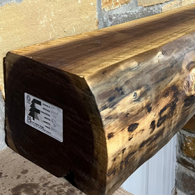 A live edge style fireplace mantel, made from walnut wood, mounted to a rock wall.