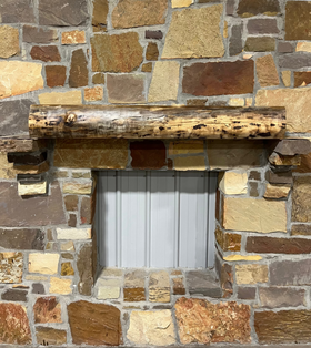 A live edge style fireplace mantel, made from walnut wood, mounted to a rock wall.