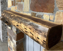 A live edge style fireplace mantel, made from walnut wood, mounted to a rock wall.