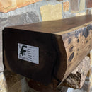 A live edge style fireplace mantel, made from walnut wood, mounted to a rock wall.