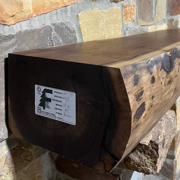 A live edge style fireplace mantel, made from walnut wood, mounted to a rock wall.