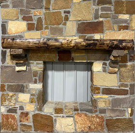 A live edge style fireplace mantel, made from walnut wood, mounted to a rock wall.