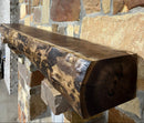 A live edge style fireplace mantel, made from walnut wood, mounted to a rock wall.