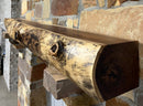 A live edge style fireplace mantel, made from walnut wood, mounted to a rock wall.